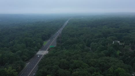 aerial footage travels over the trees alongside a suburban highway into the morning fog