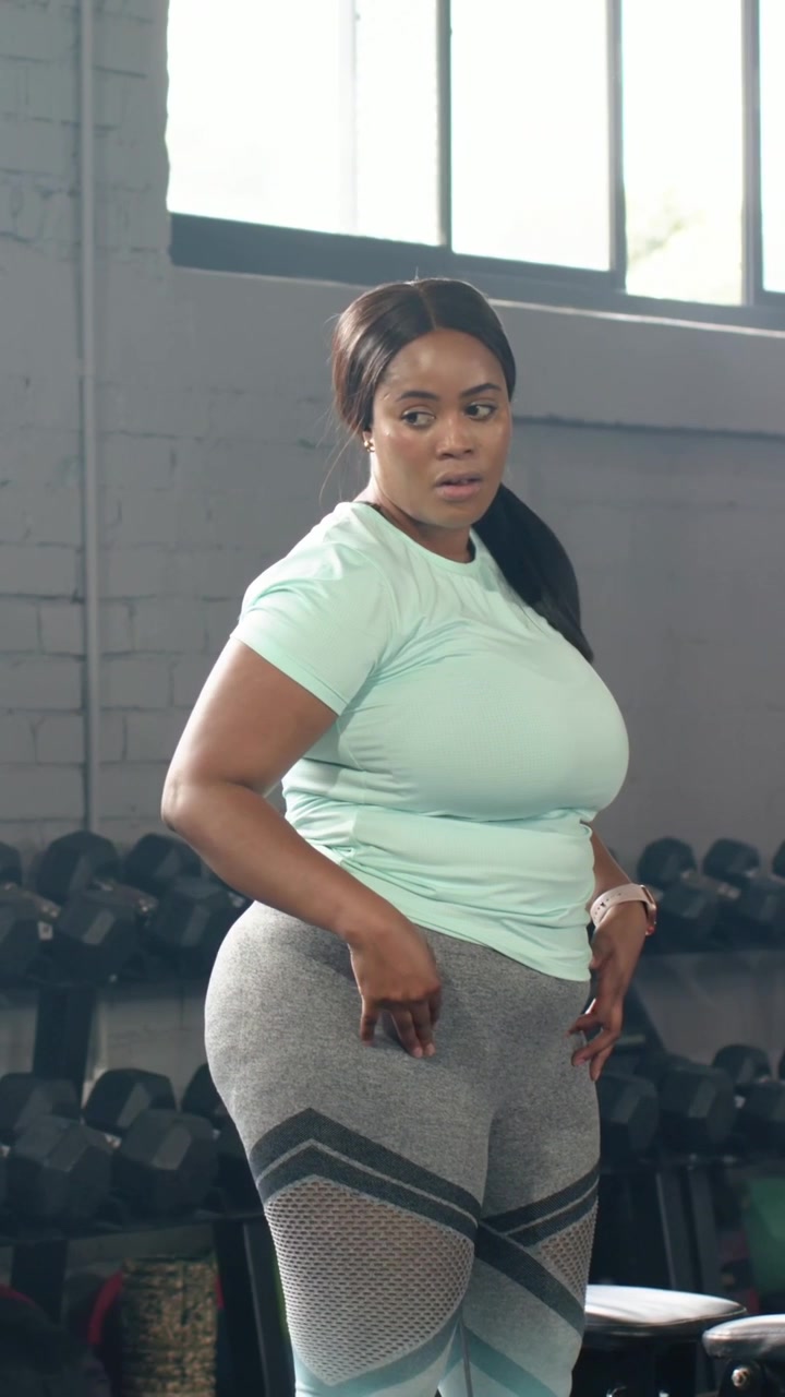 Video verticale: Donna in top color menta e leggings che si sistema l'abbigliamento in palestra, preparandosi per un set di esercizi con i pesi.