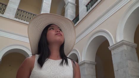 rotating shot around girl in white summer dress and hat looking around inside syros town hall