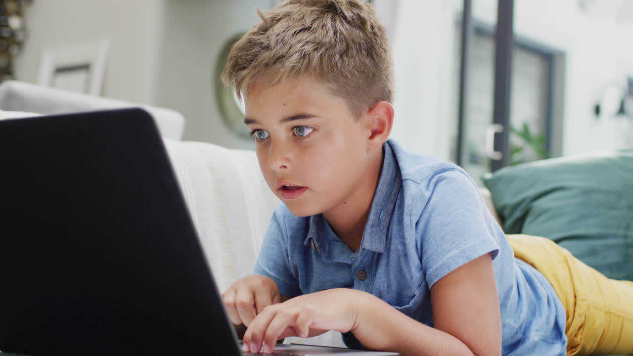 счастливый белый мальчик лежит на диване и использует ноутбук, замедленное движение