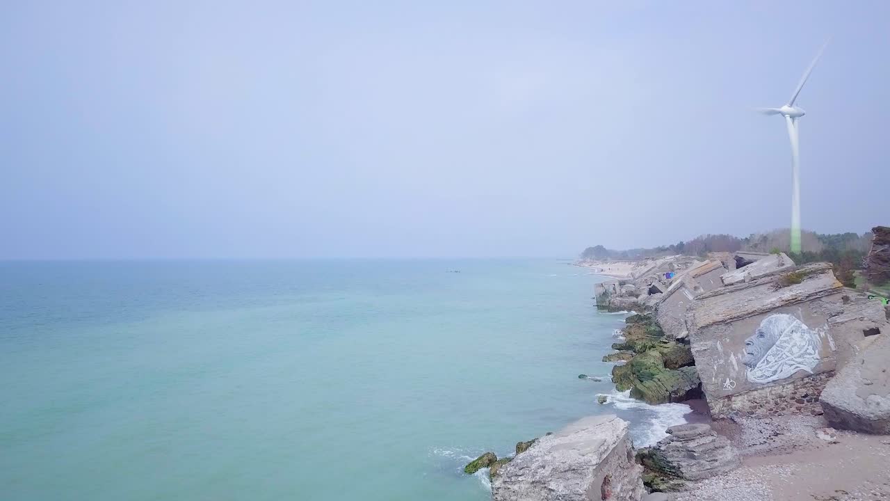 라트비아 리파야의 발트해 해변에 있는 카로스타 북부 요새에 있는 버려진 해변 요새 건물의 공중 전망, 화창한 날 잔잔한 바다, 광각 드론 샷이 앞으로 이동