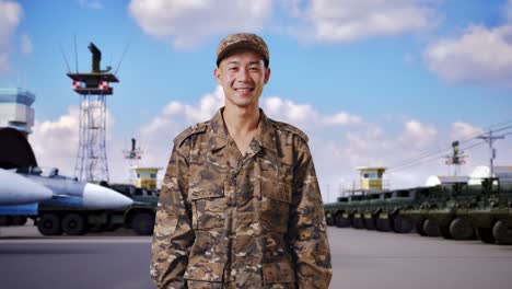 soldado hombre asiático de pie y sonriendo a la cámara en el campamento militar