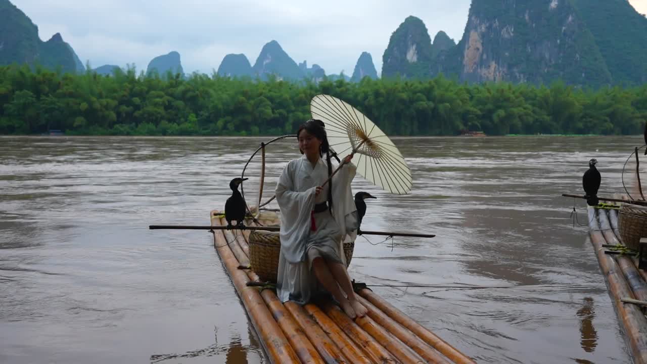 Hanfu-pige med paraply på bambusflåde i Xingping, der poserer med skarver.