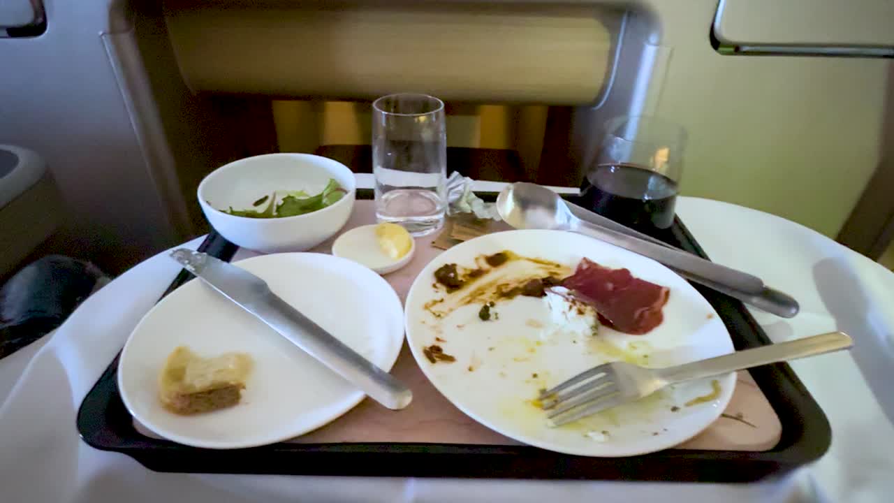 Empty dishes and utensils on airplane tray table, ambient cabin lighting, slight camera movement visible