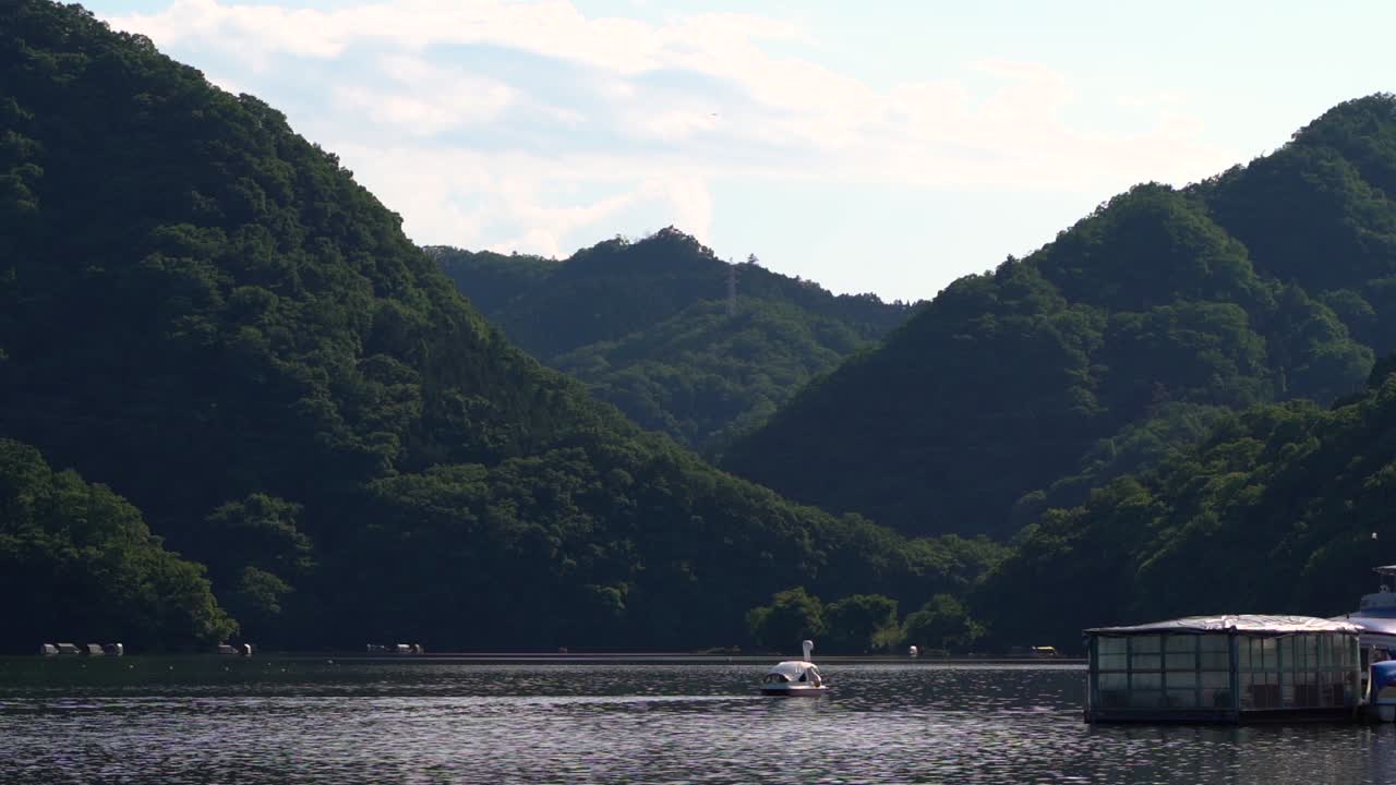 화창한 날 산 옆의 아름답고 잔잔한 호수에서 백조 보트 - 와이드 샷