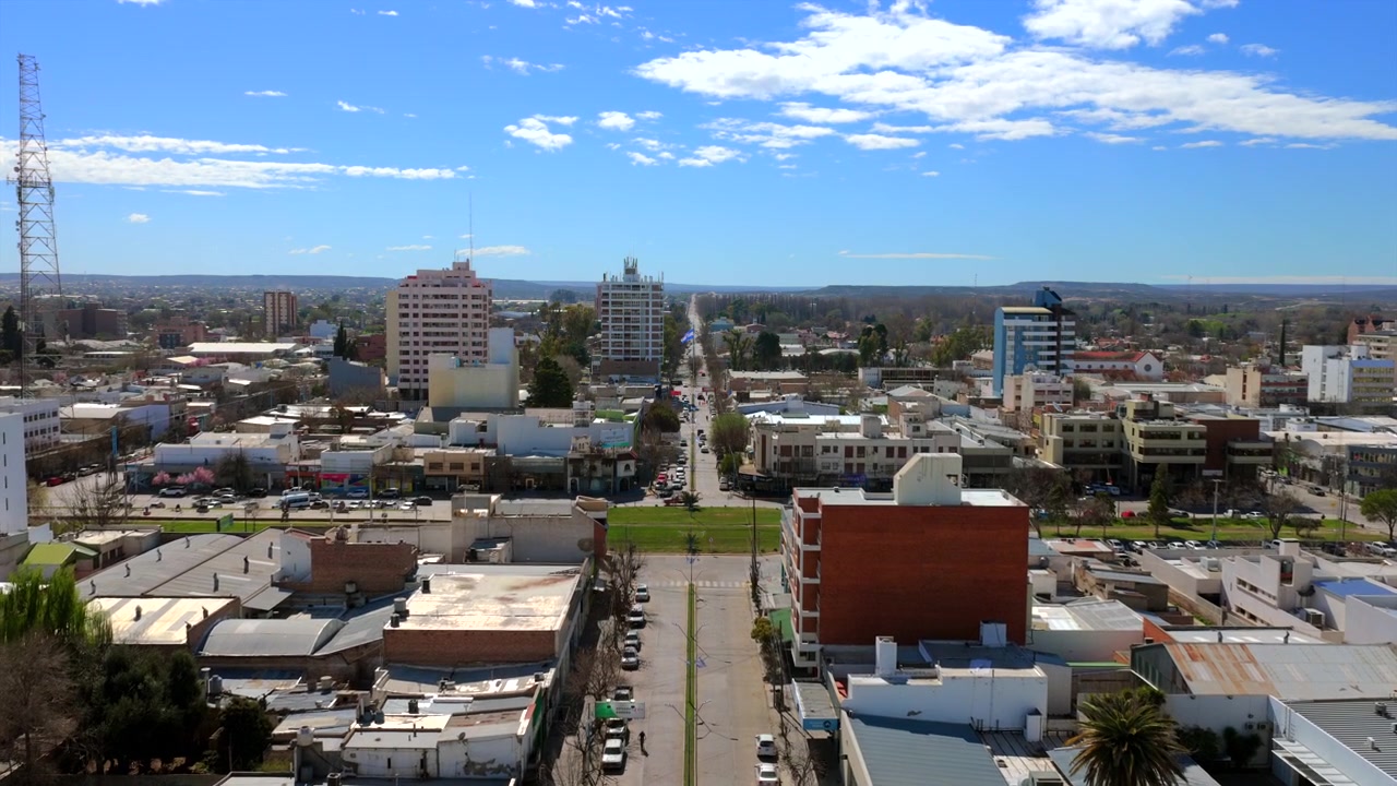 Drone sobe e avança sobre o centro da cidade de General Roca, revelando uma praça repleta de lojas locais