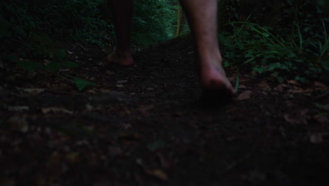 closeup of mans feet walking barefoot in slow motion down a path in an dark forrest