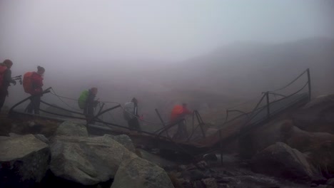 a group of hikers crossing a broken bridge on a foggy mountain