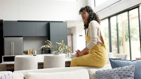 Portrait-of-happy-mature-caucasian-woman-with-long-curly-hair-sitting-on-couch-at-home,-slow-motion