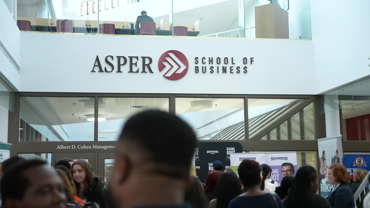 Interior sign of Asper School with students walking to class during daytime