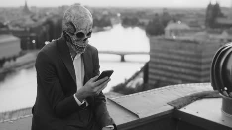 man in skull mask on city rooftop using smartphone