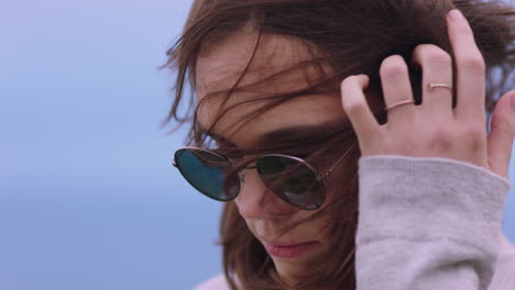 retrato de una hermosa mujer caucásica con gafas de sol disfrutando de una tranquila playa al atardecer buscando contemplativa corriendo la mano a través del cabello