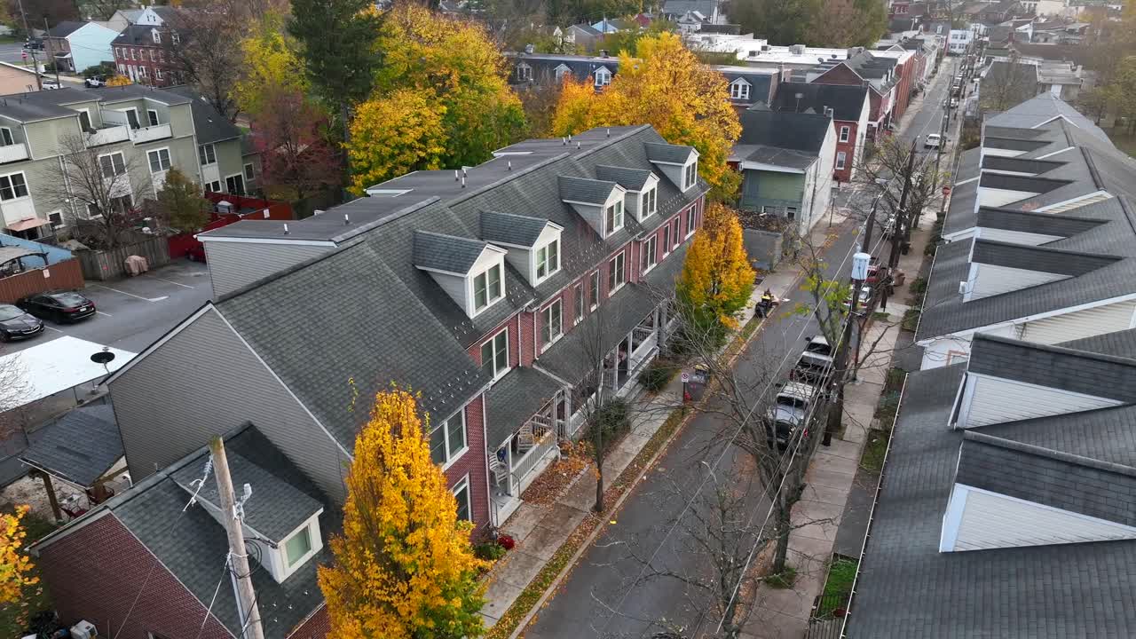 가을에 밝은 노란색 잎으로 둘러싸인 도시 교외의 타운하우스를 아래로 기울이면 공중 상승 샷