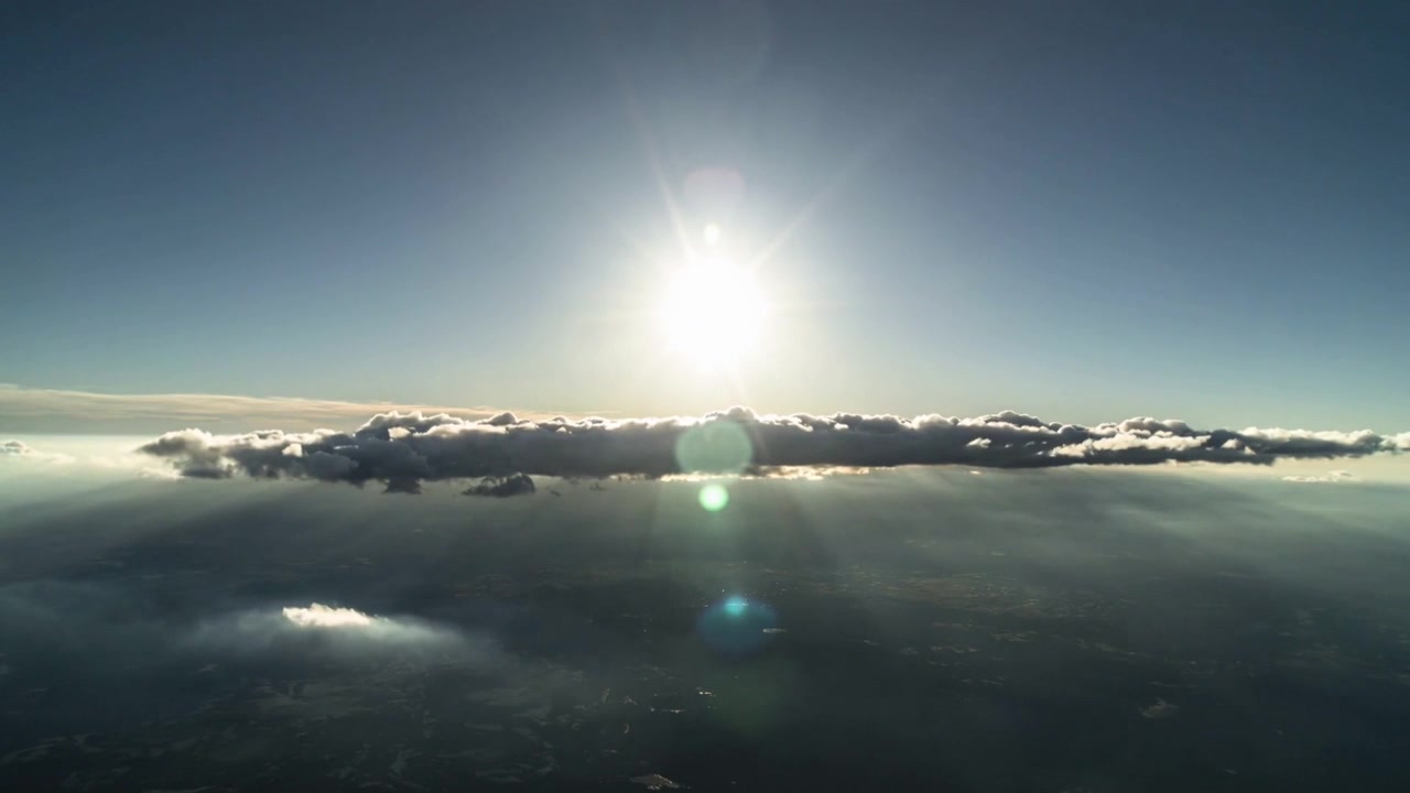 Aereo che si sposta, causando un sole splendente che proietta bagliori dell'obiettivo mutevoli su un banco di nuvole e un terreno nebbioso.