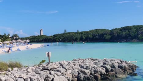 Panorámica-De-árboles,-Rocas-Y-Una-Playa-De-Arena-Con-Sombrillas,-Tumbonas-Y-Gente-En-Un-Día-Soleado-Y-Brillante-En-Las-Bahamas,-Isla-De-La-Laguna-Azul-|-4k-30fps