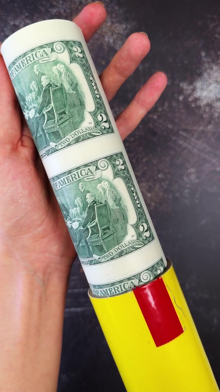 Elinde rulo yapılmış, kesilmemiş iki dolarlık banknot tabakası tutan el. Para hediye konsepti.