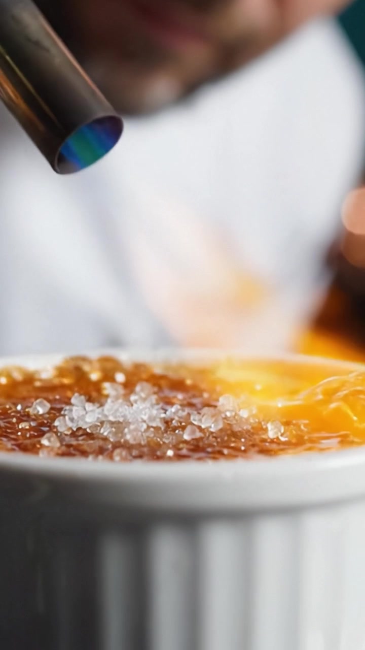 A close-up view of a deliciously caramelized dessert topped with crystals, highlighting the textures and steam rising from the warm, sweetened surface.