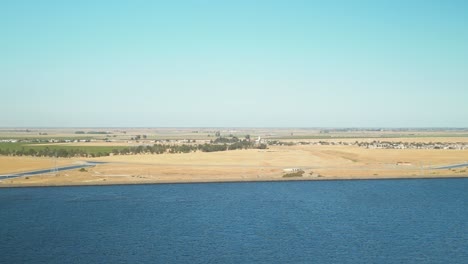 a sweeping drone flight over the shimmering waters of san luis reservoir, framed by vast open landscapes and rugged hills under the afternoon sun in merced county, california, usa.