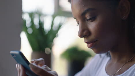 mujer afroamericana feliz usando un teléfono inteligente en un café navegando por mensajes en línea disfrutando de compartir su estilo de vida en las redes sociales relajándose en un restaurante de cafetería de cerca