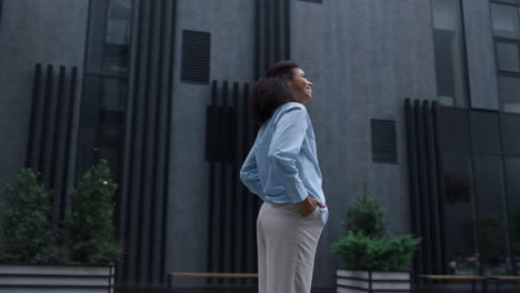 Smiling-woman-standing-at-modern-office-building-looking-in-camera.-Proud-winner