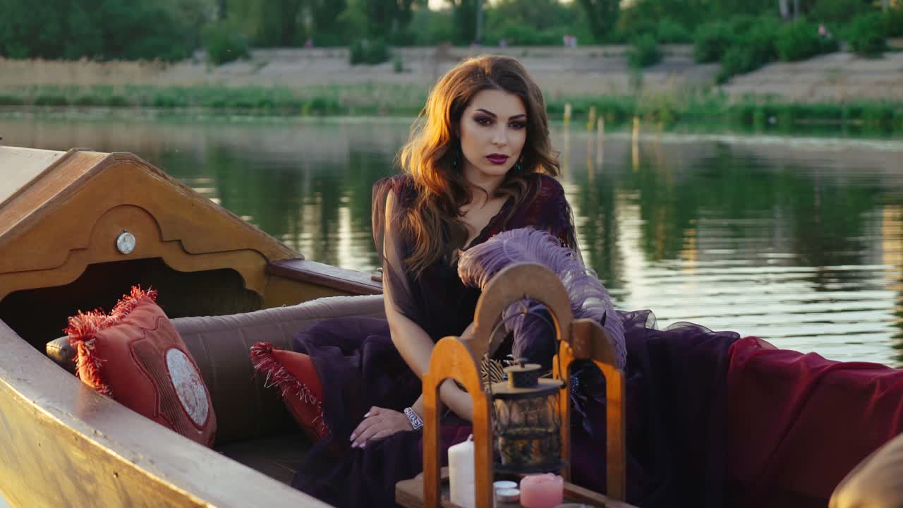 A gorgeous lady sitting and looking around herself in the boat in the middle of the river in a purple dress on a blurred background. Carnival