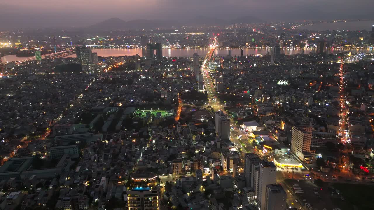 Panorama aereo con drone del centro della città di Da Nang, Vietnam, diviso dal fiume Han, skyline illuminato di notte con autostrada trafficata