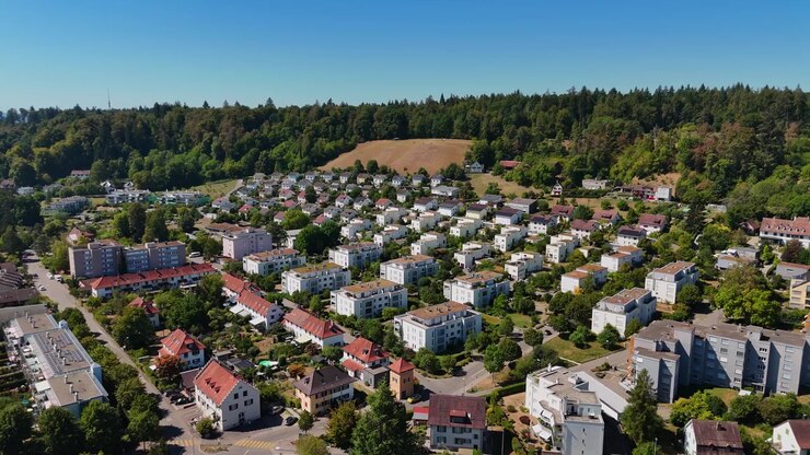 Luftaufnahme über einem Hangwohnviertel in Schaffhausen, Schweiz, zeigt Wohnblöcke, Einfamilienhäuser, Gärten und dichtes Waldgebiet an einem klaren Sommertag
