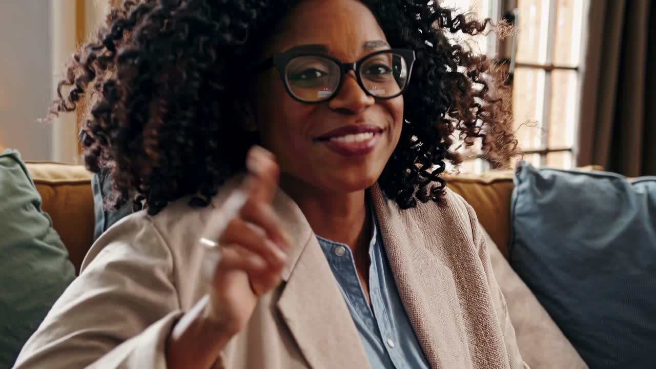 Close-up video shot of a smiling person in glasses and a beige blazer, capturing a warm