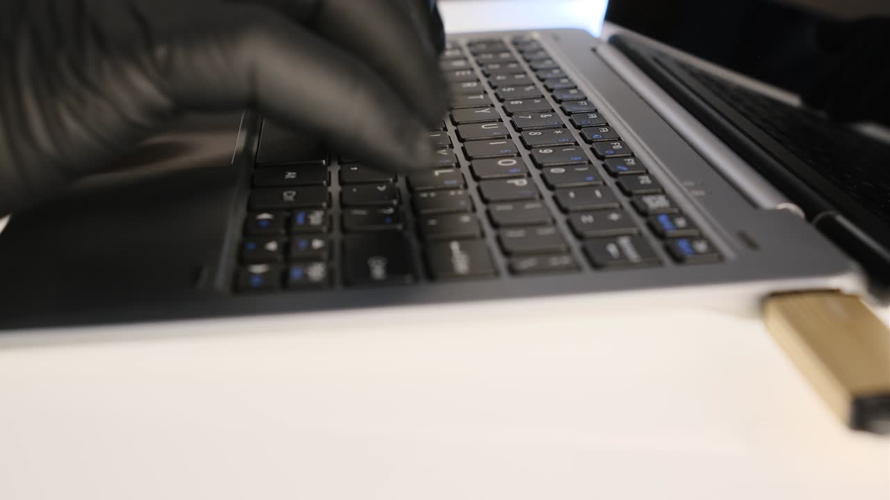 hacker escribiendo en una computadora portátil con guantes negros y copiando datos en una unidad flash usb