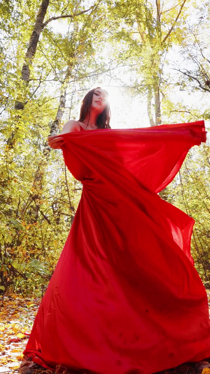 Uma Dançarina Graciosa em um Vestido Vermelho Esvoaçante Iluminada pela Luz do Sol Entre a Folhagem de Outono, Exibindo Elegância e Movimento no Brilho Dourado da Natureza