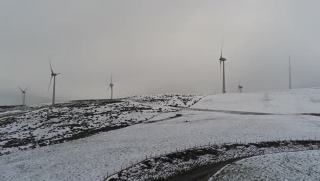 Winter-mountain-countryside-wind-turbines-on-rural-highlands-aerial-view-cold-snowy-valley-hillside-left-pull-back-slow