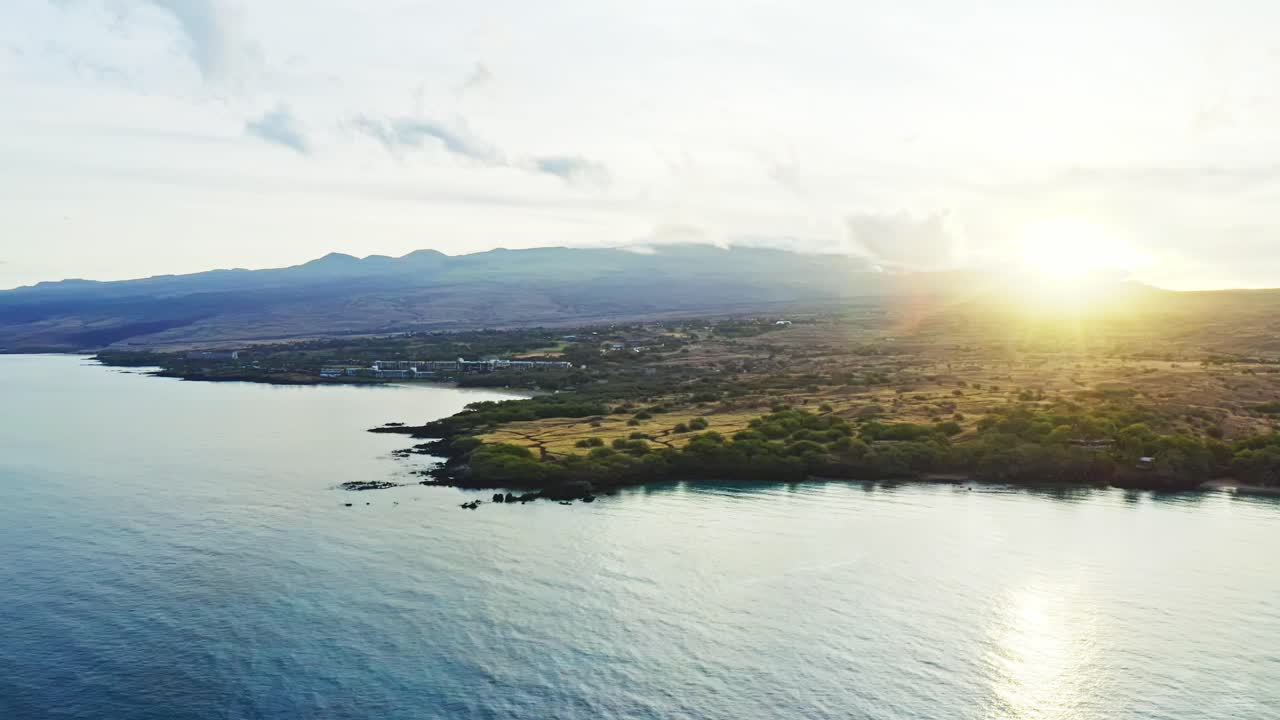 The early sun rises over Hawaii’s volcanic slopes, casting a warm golden glow across the coastline where the Pacific’s tranquil waters meet the island’s untamed land
