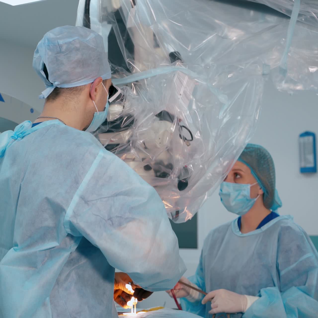 Surgeon and medical nurse looking in a large microscope. Surgeons in medical uniform and masks perform an operation in the contemporary operating room. Neurosurgery.