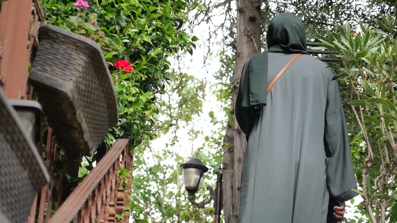 женщина в хиджабе поднимается по лестнице в саду