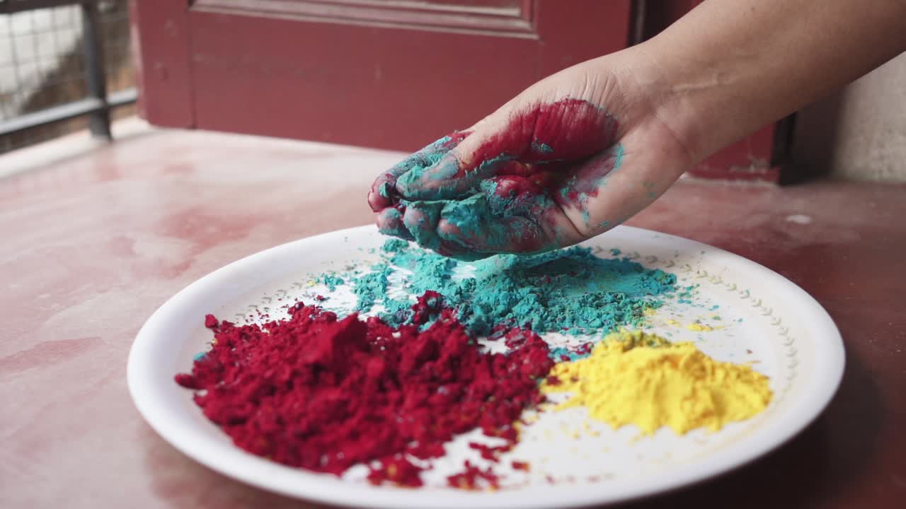Mano che gioca con polveri colorate su un piatto durante Holi, festa indiana, a casa a causa del lockdown per il COVID-19. Primo piano cinematografico, in slow motion.