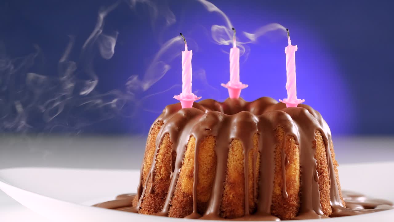 soplando velas de cumpleaños rosas en pastel de mármol con glaseado de nougat de chocolate