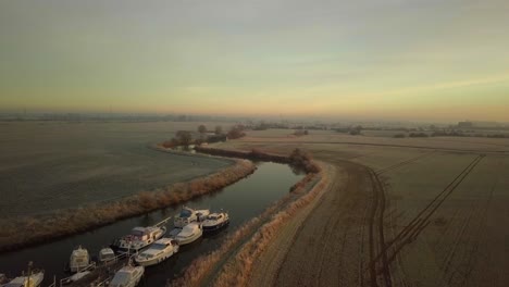 Drone-flies-over-meandering-river-and-frosty-fields-with-sunrise-behind-drone