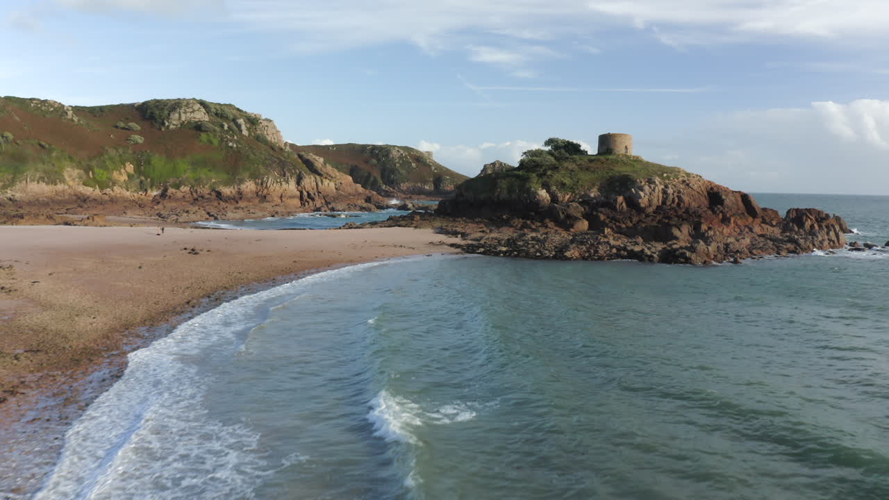 una toma aérea de avance de la playa de portelet en la costa sur de jersey con la playa de arena y la torre de portelet