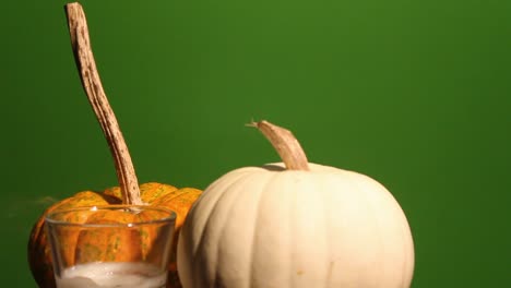 la llama de una vela se apaga frente a dos calabazas con fondo de pantalla verde
