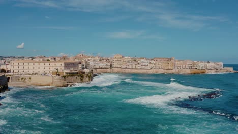aerial drone shot of ortigia, syracuse. flying along the coast of ortigia island with large waves crashing on the shore. historic italian town in sicily.