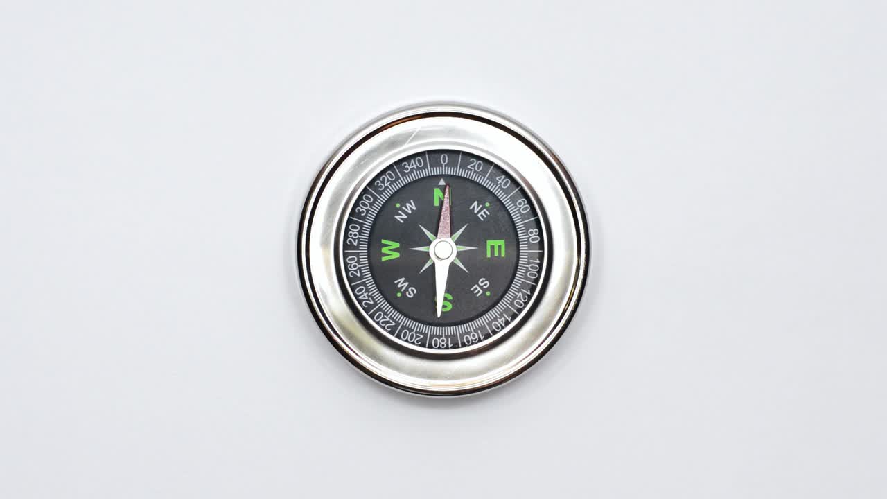 Closeup shot of round magnetic compass with silver frame placed on clean white surface in West Virginia, America, showing cardinal directions and degrees for accurate navigation
