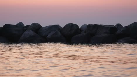 sunset over water sea, line of rocks in water, dusk light