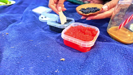 mujer saca caviar de huevos de salmón con huevos rojos y negros mientras lo extiende sobre el pan en la manta de picnic