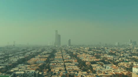 aerial over housing with bahria icon tower in the distance in karachi covered in smog. pedestal up