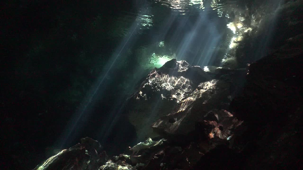 los rayos del sol brillan a través de la superficie del agua sobre la formación rocosa en el sistema de cuevas del cenote chikin ha, yucatán, méxico.