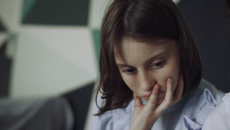 Portrait-serious-schoolgirl-looking-down-sitting-corridor.-Child-leaning-on-hand