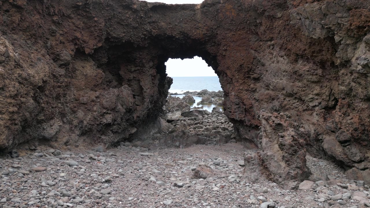Vista dall'interno dell'arco di una dolina vulcanica, con il pavimento roccioso che conduce verso l'oceano