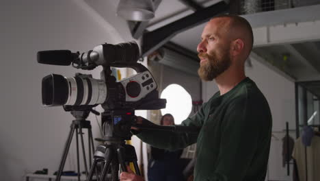 male film camera operator focusing lens on camera mounted on tripod shooting movie or video in studio