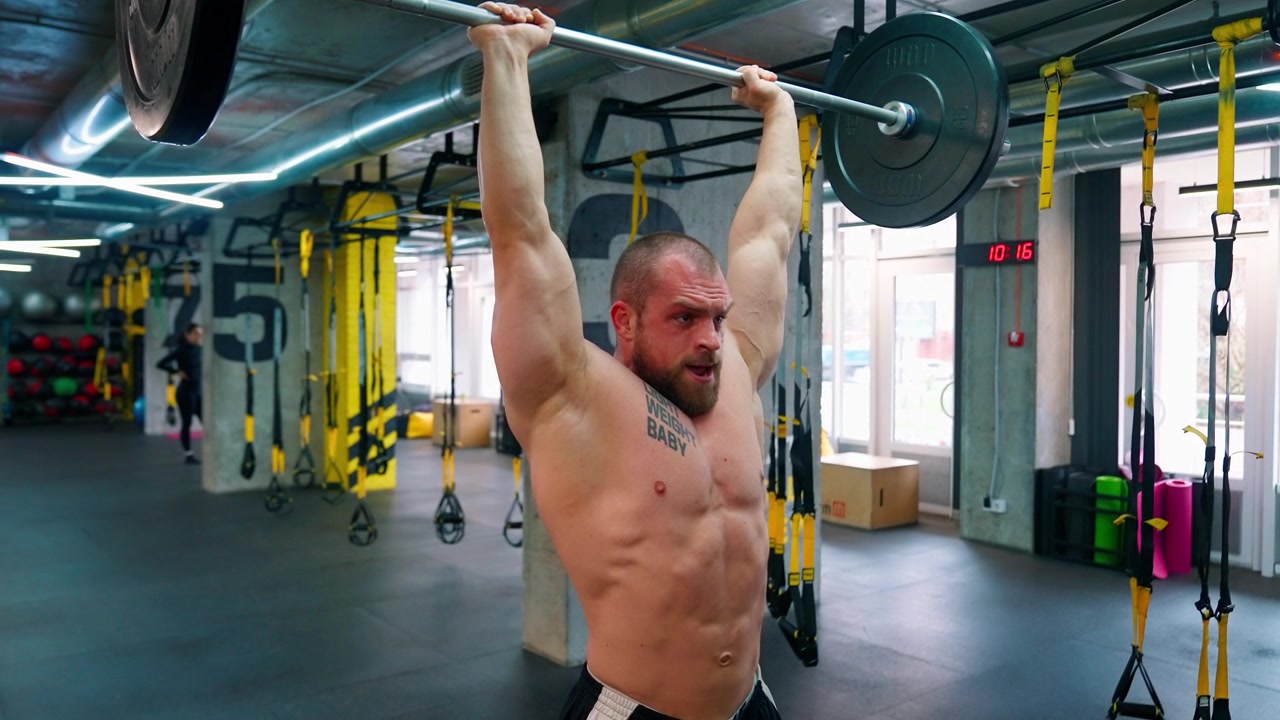 Uomo muscoloso che esegue un'overhead press con bilanciere in una palestra moderna