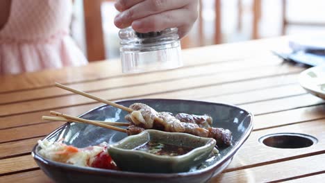 person seasoning food with a shaker over a plate